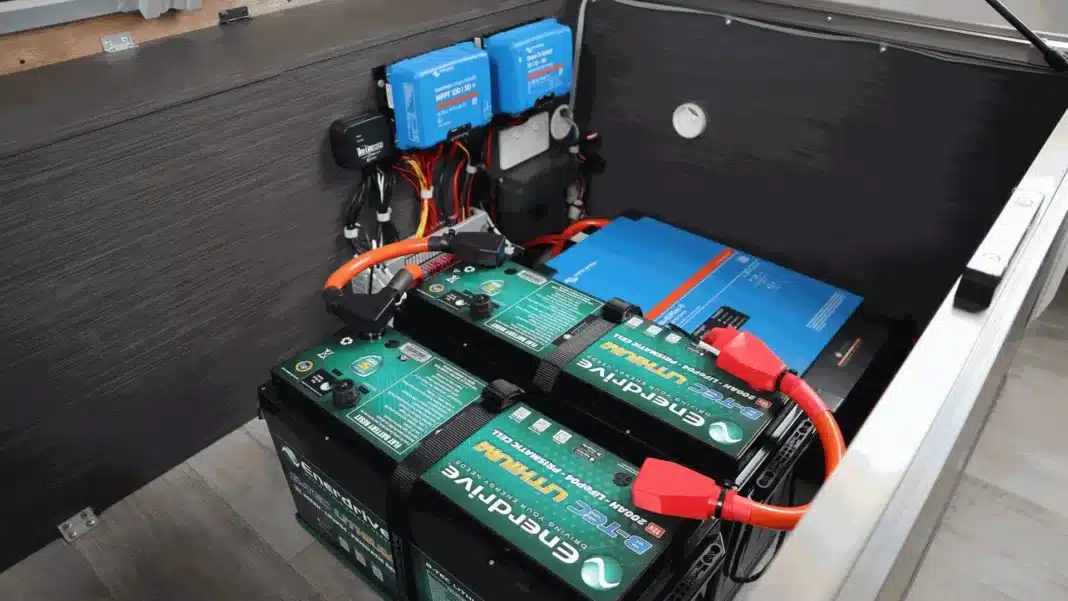 Two lithium batteries strapped into a caravan battery compartment, wired to blue Victron solar controllers and an inverter