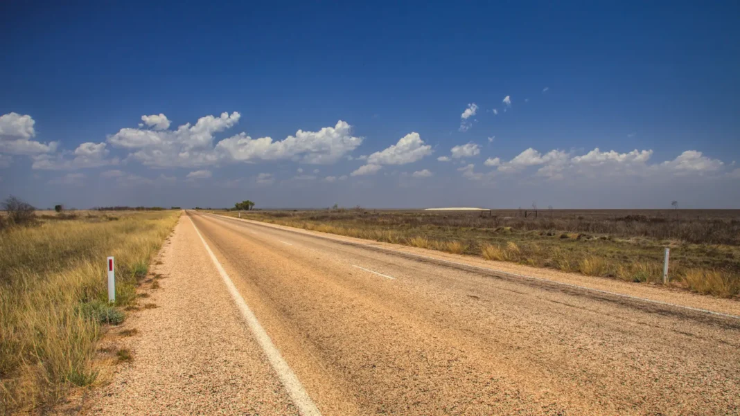highway-south-of-broome-red-verges Long straight sealed highway with white edge lines running through flat dry grassland under scattered cloud