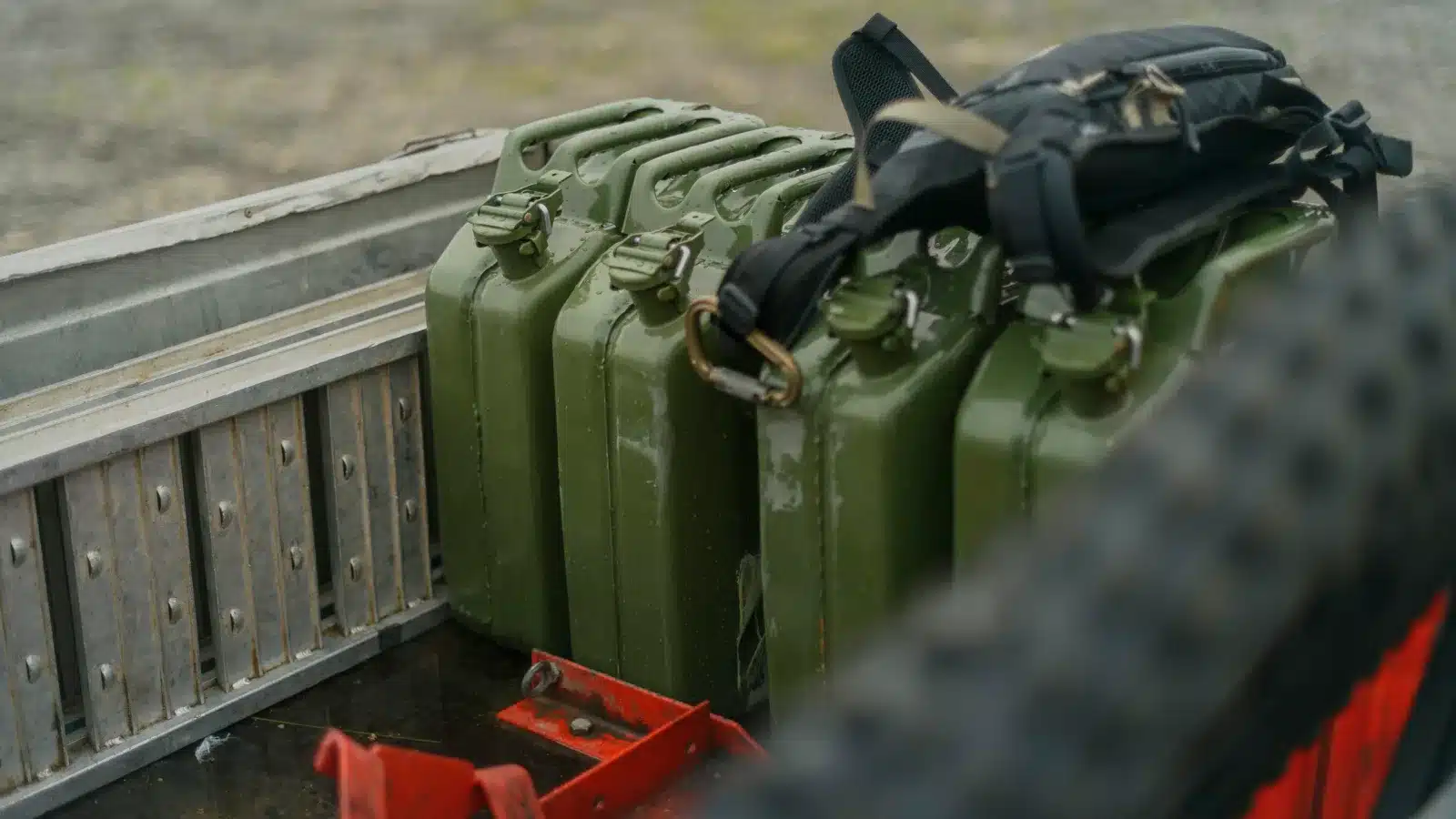 Three green metal jerry cans and a backpack strapped in the tray of a ute