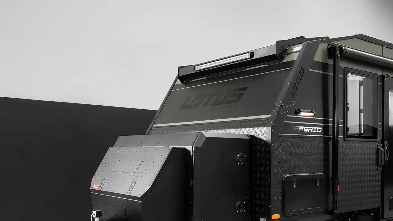 Lotus Off Grid off-road caravan with black cladding and a front toolbox, photographed in a studio