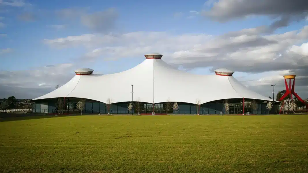 White tent-like roof of the Grand Pavilion at Melbourne Showgrounds behind a wide green lawn