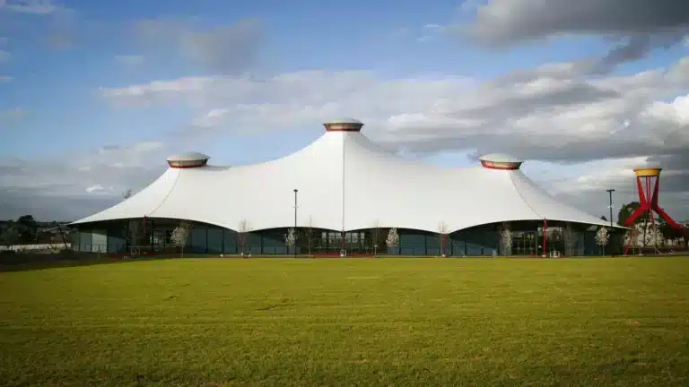 White tent-like roof of the Grand Pavilion at Melbourne Showgrounds behind a wide green lawn