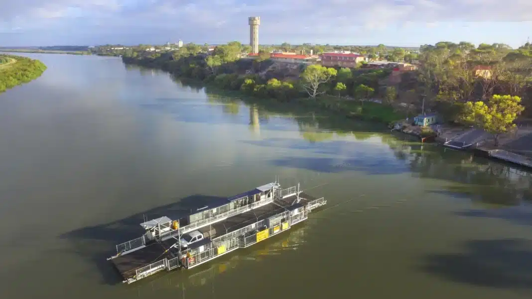 Aerial view of a cable ferry carrying a car across a wide stretch of the Murray River below Tailem Bend and its water tower