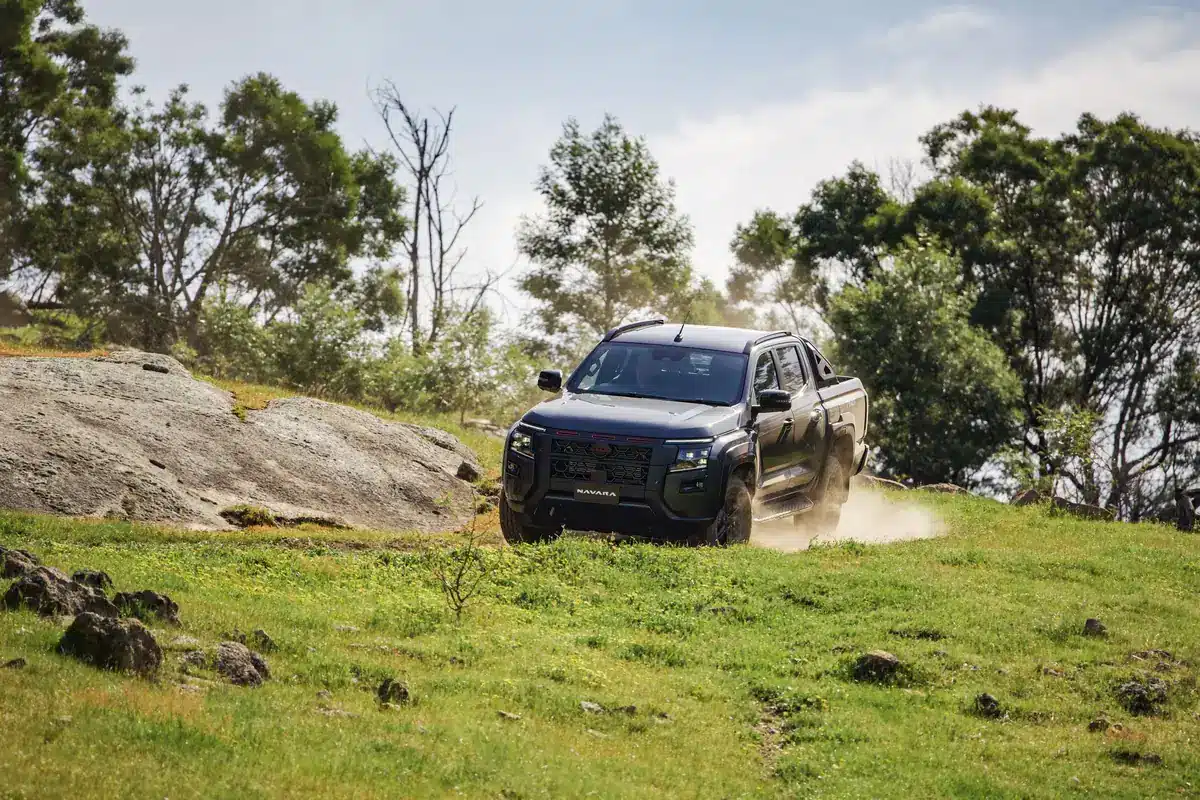 Dark grey 2026 Nissan Navara PRO-4X dual cab climbing a grassy hill past granite boulders
