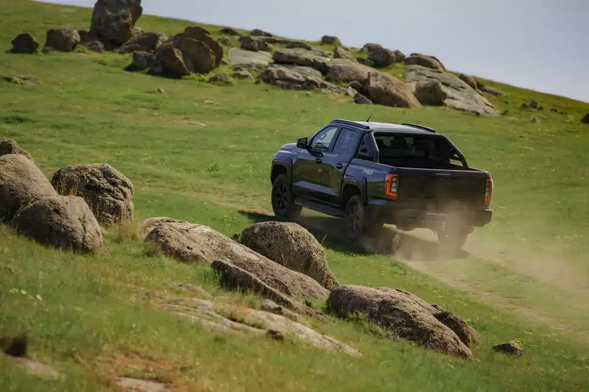 Rear view of a dark grey 2026 Nissan Navara PRO-4X driving up a rocky grassy slope
