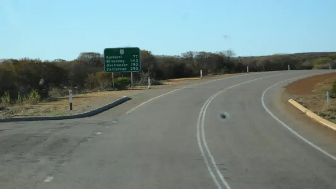 north-west-coastal-highway-north-of-northampton North West Coastal Highway curving past a green distance sign listing Kalbarri, Billabong, Overlander and Carnarvon