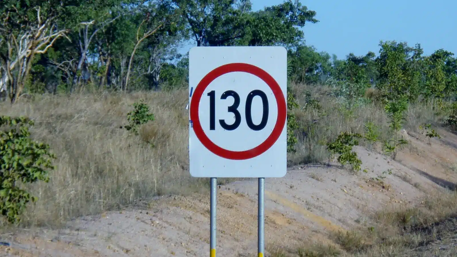 Northern Territory 130km/h speed limit sign on the roadside, set against scrub and a dirt embankment