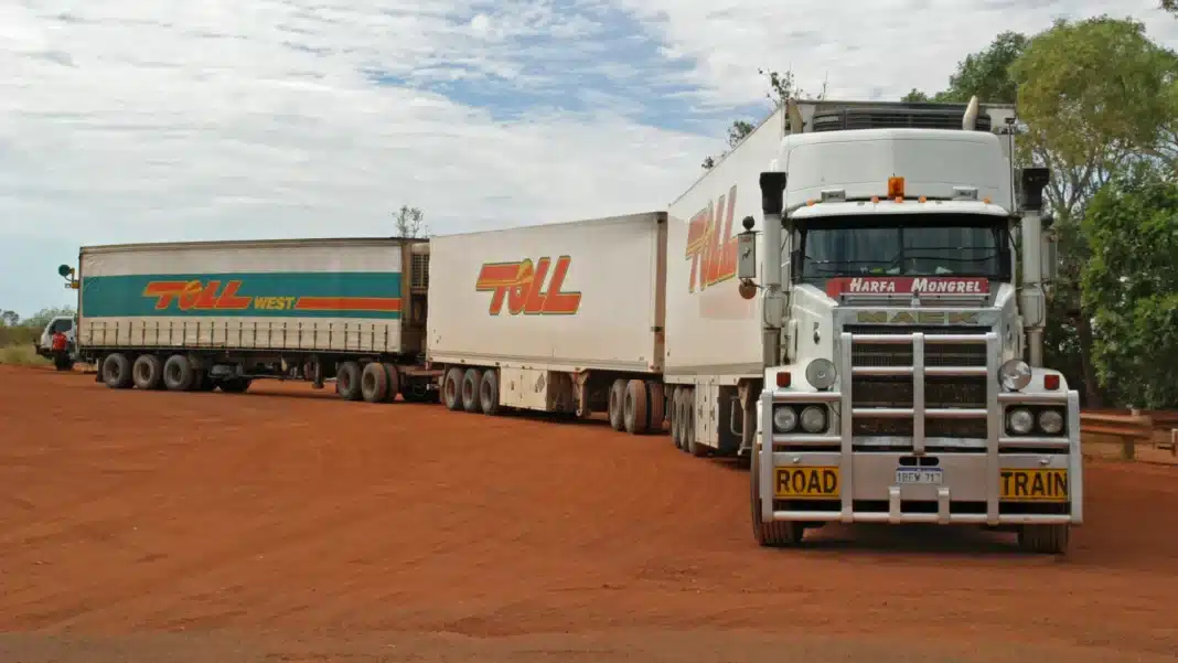 road-train-great-northern-highway-wa Triple road train with a white prime mover parked on red gravel beside trees in Western Australia