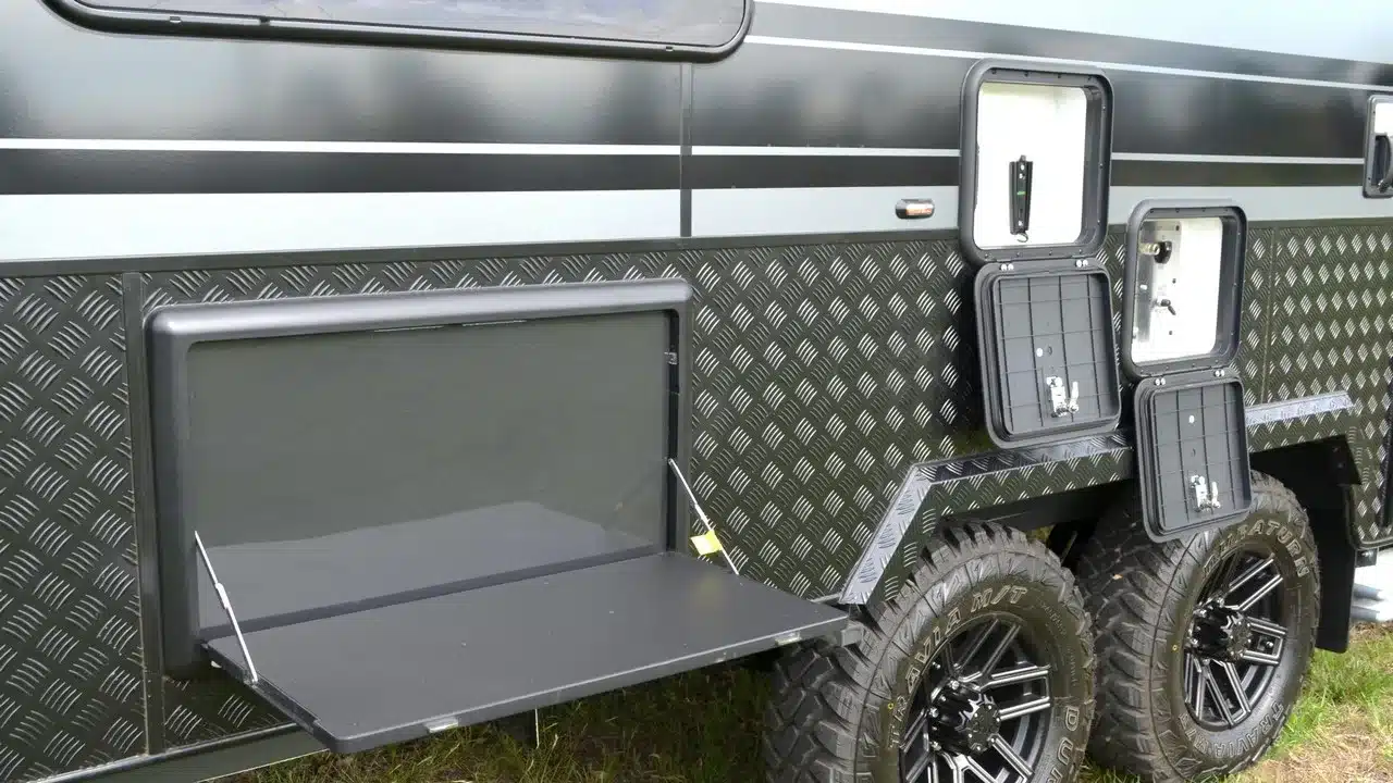 Salute Garrison off-road caravan with diamond-plate cladding, a fold-down table and open service hatches on its side