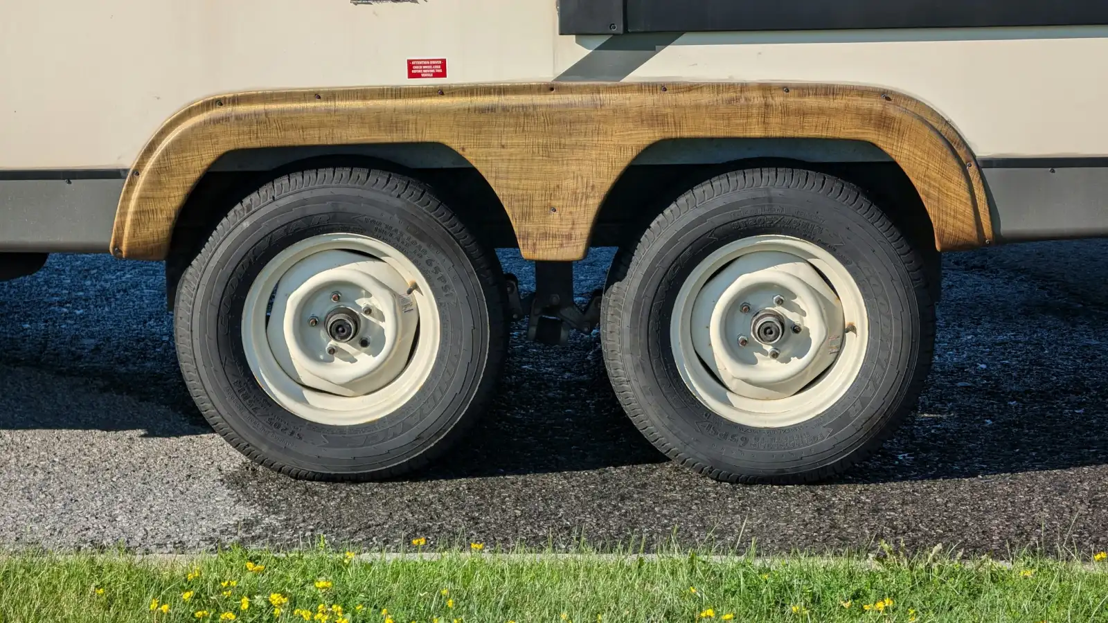Tandem axle wheels and timber-look wheel arch of a caravan parked on a gravel roadside