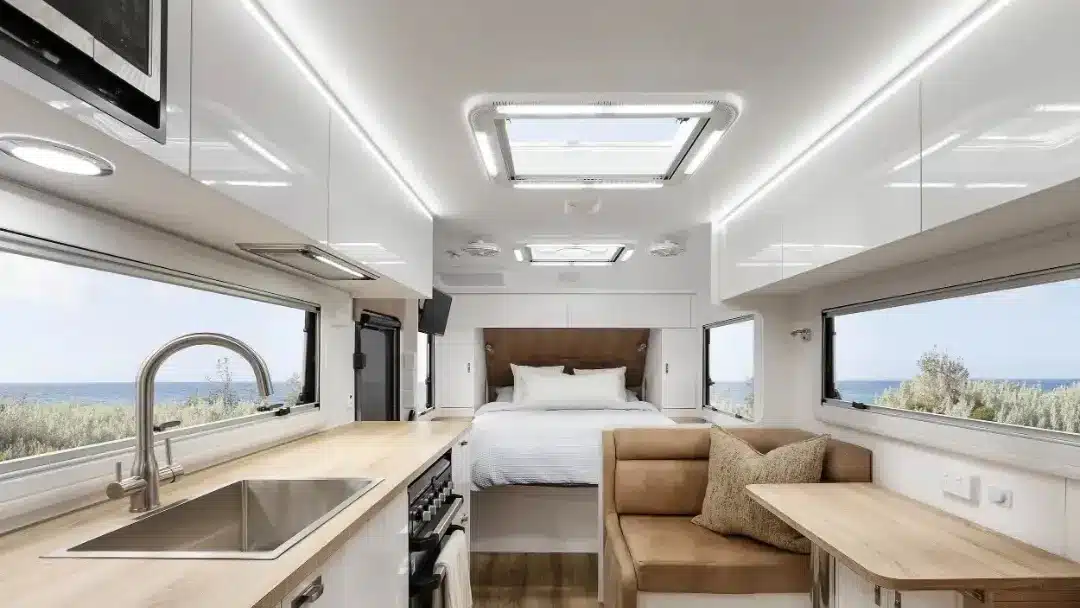 Interior of a Titanium S4 caravan with white cabinetry, timber benchtops, a kitchen sink and a bed at the far end