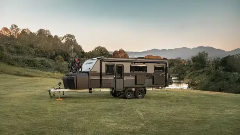 Titanium S4 off-road caravan with bikes on the drawbar, parked on a grassy rise at dusk with hills behind