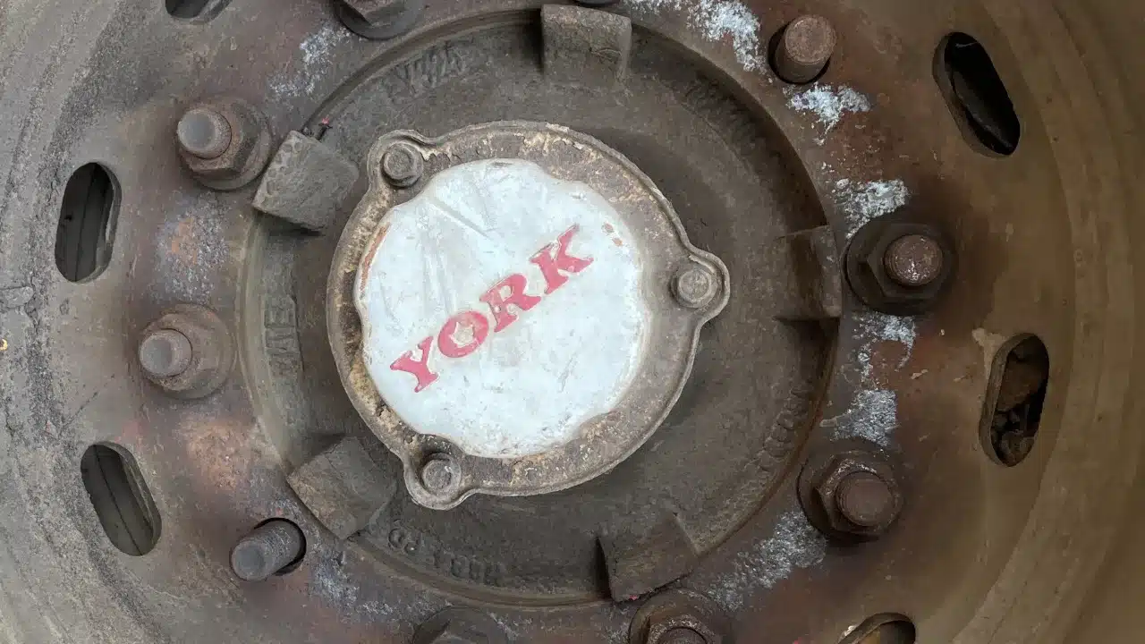 Close-up of a rusty heavy-trailer wheel hub with a York hub cap and wheel nuts