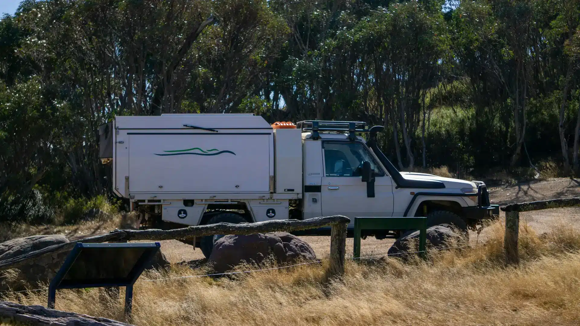 ute-hitched-to-off-road-caravan-bush-camp White LandCruiser ute with a camper canopy and roof rack parked on dry grass at a bush camping area