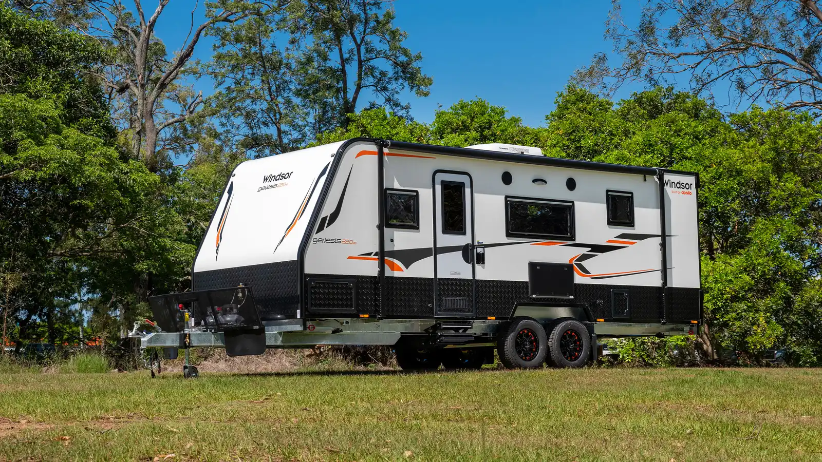 White Windsor Genesis 220MD caravan with orange decals parked on grass among trees